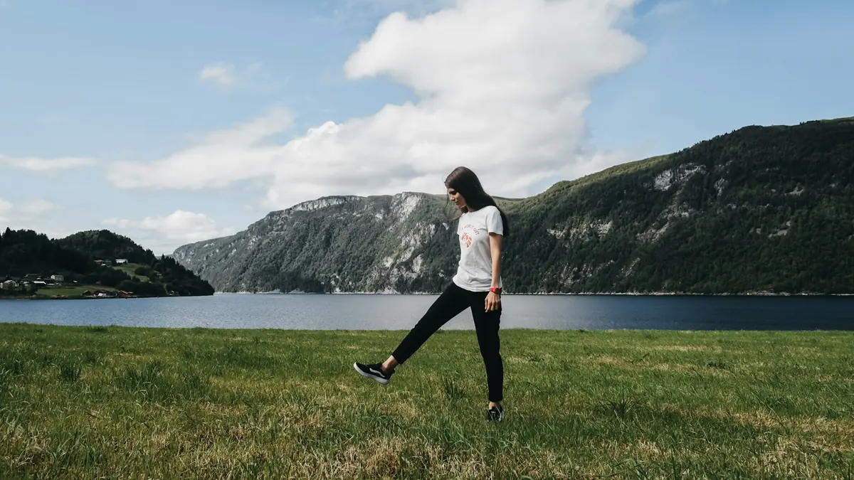 En kvinne går lett på en gresslette ved en fjord en sommerdag.