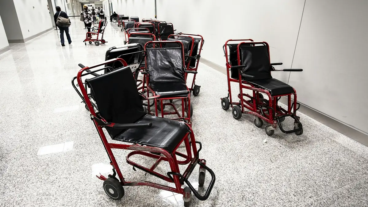 Rekker med transportrullestoler står parkert langs en lang, lys korridor.