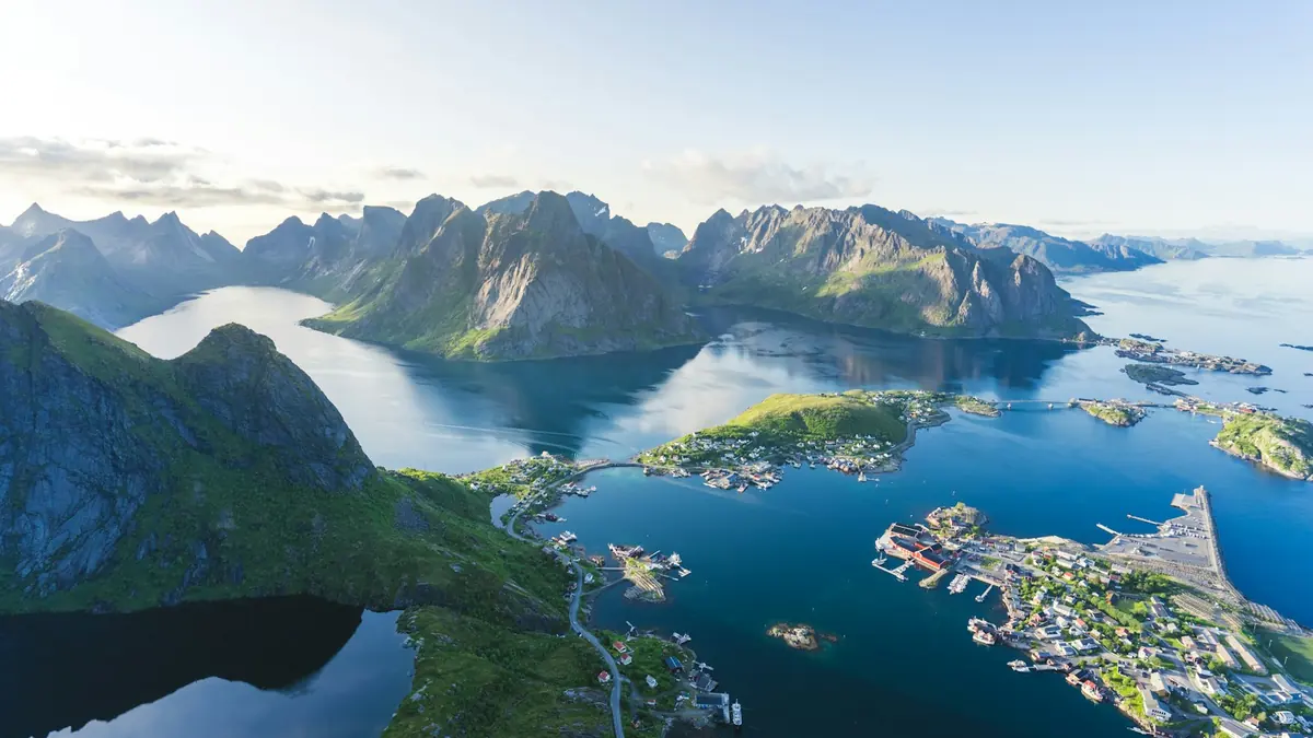Utsikt over et norsk kystsamfunn med hus, broer og fjell rundt fjorden en klar sommerdag